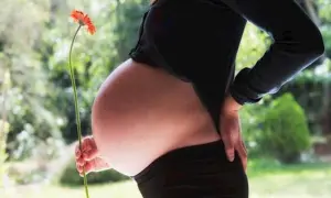 Ciąża w 3 trymestrze. Brzuch ciężarnej z kwiatkiem w dłoni, symbolizującym nowy początek.