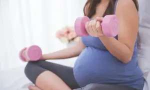 Ciężarna kobieta ćwiczy z różowymi hantlami, przygotowując się do porodu.