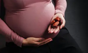 Kobieta w ciąży trzyma w dłoni garść daktyli.