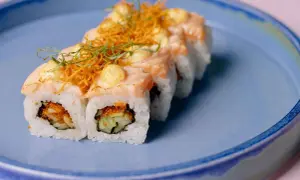 Rolka sushi z łososiem i warzywami na niebieskim talerzu. Czy w ciąży można jeść sushi? To pytanie nurtuje wiele przyszłych mam.