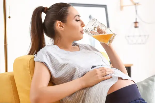 Kobieta w ciąży relaksuje się na kanapie, pijąc piwo bezalkoholowe.