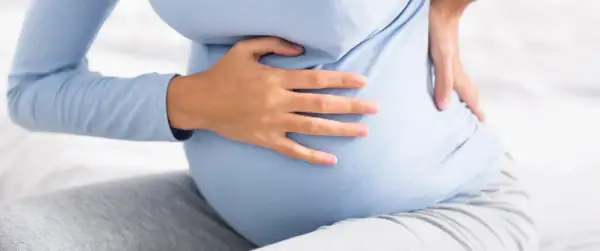 Kobieta w ciąży trzyma się za bok, odczuwając ból sugerujący kolkę nerkową w ciąży.