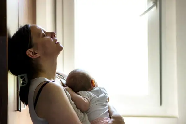 Zmęczona mama tuli śpiące dziecko. Czas po porodzie bywa trudny, ale miłość do malucha daje siłę.