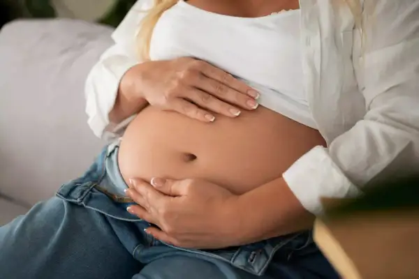 Kobieta w ciąży delikatnie dotyka brzucha. To intymny moment, który może obejmować masturbację w ciąży, jako formę dbania o siebie.