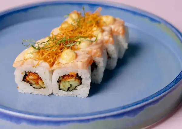 Rolka sushi z łososiem i warzywami na niebieskim talerzu. Czy w ciąży można jeść sushi? To pytanie nurtuje wiele przyszłych mam.